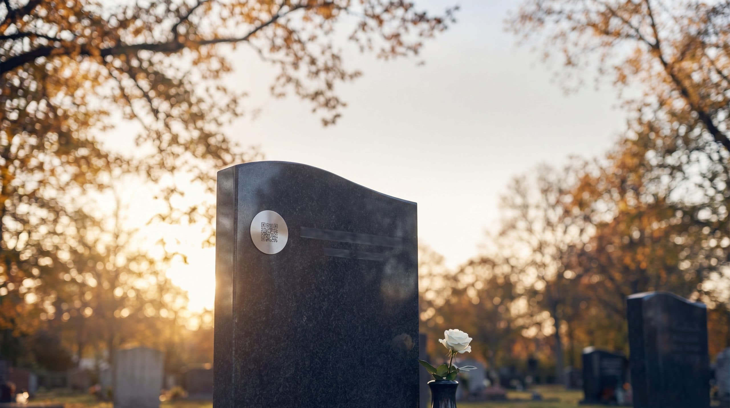 A modern granite headstone in a peaceful cemetery setting at golden hour — upright monument with a small QR memorial plaque visible on the polished face, soft natural light